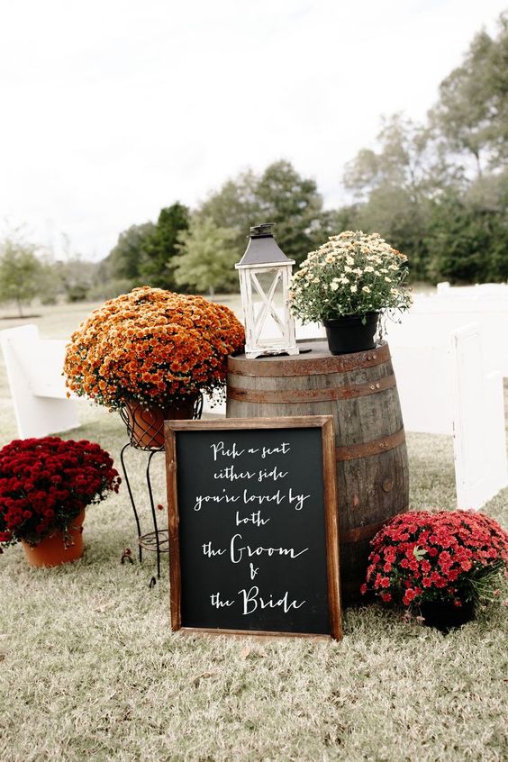 bright fall wedding decor with a barrel, bright potted blooms, a candle lantern and a chalkboard sign in a frame