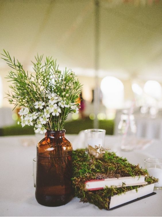 moss covered books, an amber glass vase plus wildflowers and greenery is a simple and rustic idea