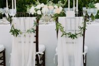white tulle chair covers with bows and some greenery for chic and elegant chair decor