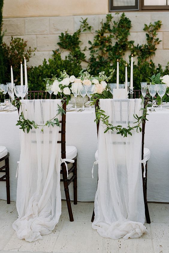 white tulle chair covers with bows and some greenery for chic and elegant chair decor
