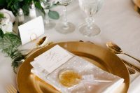 a beautiful neutral wedding tablescape with lots of greenery, blush, white and lilac blooms, a gold charger and cutlery, a gold lollipop as a favor