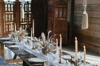 a boho lux wedding tablescape with a white runner, gold figurines, candles, dried blooms and grasses and feather balls over the table