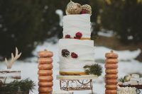 a boho rustic winter wedding cake with tiers of chocolate, gilded pinecones and pears, blooms and berries