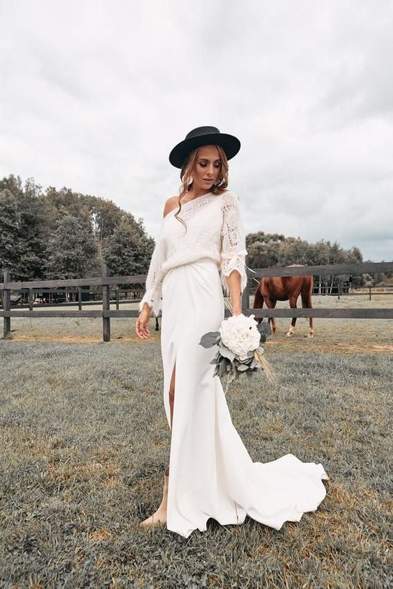 a boho winter bridal look with a crochet one shoulder sweater, a white maxi skirt with a slit and a train, tan booties and a black hat