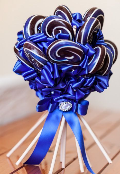 a bold and quirky wedding bouquet of blue, white and chocolate lollipops with blue ribbon and a bow