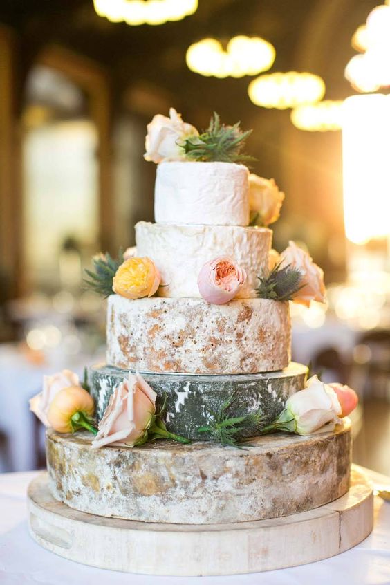 a cheese wheel wedding cake topped with peachy and blush blooms plus thistles, for a rustic spring or summer wedding