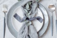 a chic minimalist wedding tablescape with a grey table runner, grey plates, eucalyptus and grey cutlery