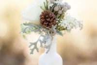 a cozy and simple winter decoration of a white bottle, pinecones, berries and white blooms plus pale millet