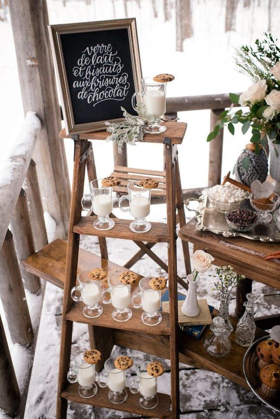 a cozy milk and cookies food and drink station with a chalkboard sign and pale millet for a rustic winter wedding