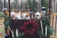 a cozy winter hot chocolate bar done with evergreens, branches, candle lanterns and some cups, chocolate and liquors