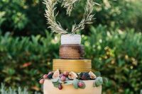 a fabulous cheese wheel wedding cake topped with greenery, figs, grapes and with a greenery heart-shaped topper for a summer wedding