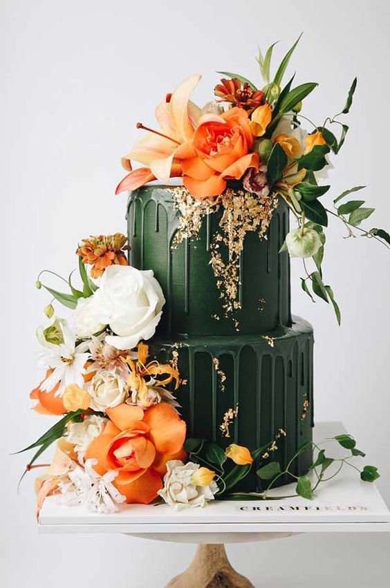 a gorgeous dark green wedding cake with matchign drip and bold orange and white blooms and greenery looks jaw-dropping