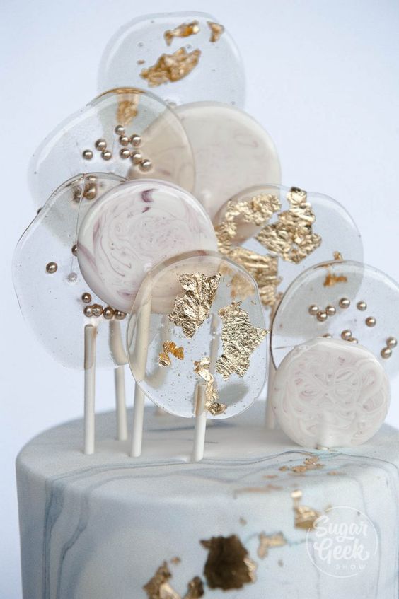 a grey marble wedding cake topped with clear and white lollipops decorated with gold is amazing