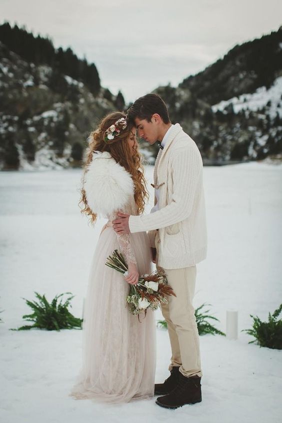 a groom rocking tan jeans, a white shirt, a white chunky cardigan and black boots for a winter boho wedding