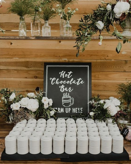 a hot chocolate bar with greenery, white blooms and a chalkboard sign is a cool idea for a rustic winter wedding