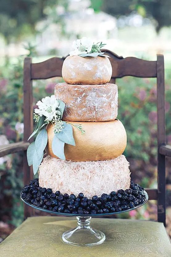 a huge cheese tower with greenery and flowers and some cherries for displaying is a lovely idea for a summer or fall wedding