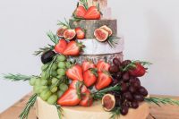 a lovely cheese wheel wedding cake decorated with grapes, strawberries and figs, herbs and a cake topper is a fantastic idea