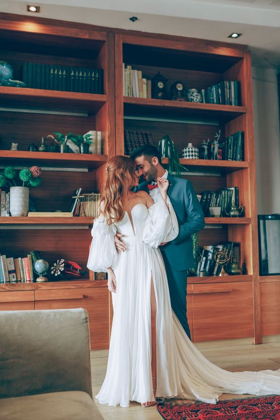 a lovely off the shoulder wedding dress with a corset bodice with a plunging neckline, puff sleeves and a pleated skirt with a front slit and a train