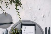 a modern wedding tablescape with greenery, candles, matte grey plates, a black napkin and greenery