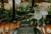 a moody winter wedding tablescape with an evergreen runner, black candles, black plates and an elegant black and copper paper goods