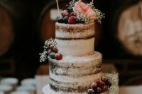 a naked wedding cake topped with blooms, sugared berries, banners for a rustic wedding