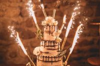 a naked wedding cake with chocolate drip, white blooms and greenery and sparklers is a lovely idea for a boho wedding