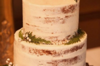 a naked wedding cake with evergreens, berries and pinecones on a wood slice for a rustic winter wedding