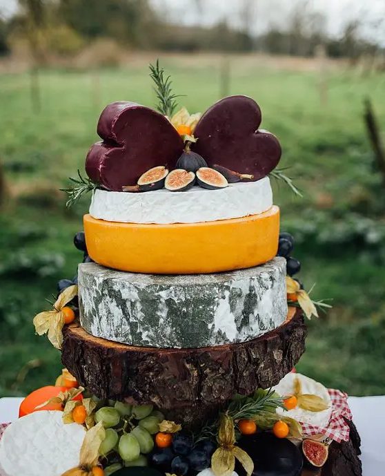 a rustic cheese tower on a thick wooden piece with herbs and figs plus a duo of dark heart-shaped cheese pieces is a fantastic idea for a rustic wedding