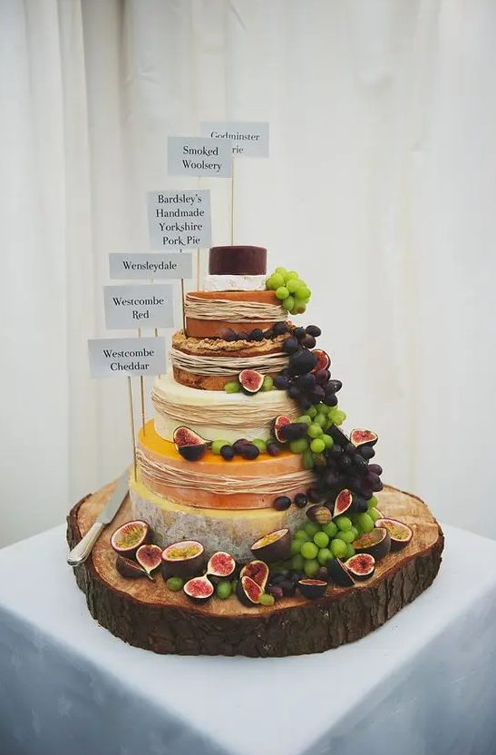 a rustic display with grapes, figs, straw and toppers and gorgeous cheese wheels on an oversized wooden slice for a rustic wedding