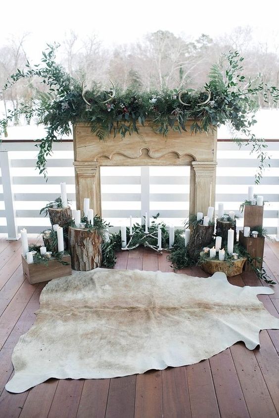 a rustic wedding ceremony backdrop of a faux mantel, greenery, antlers, tree stumps with candles and antlers and a fur rug