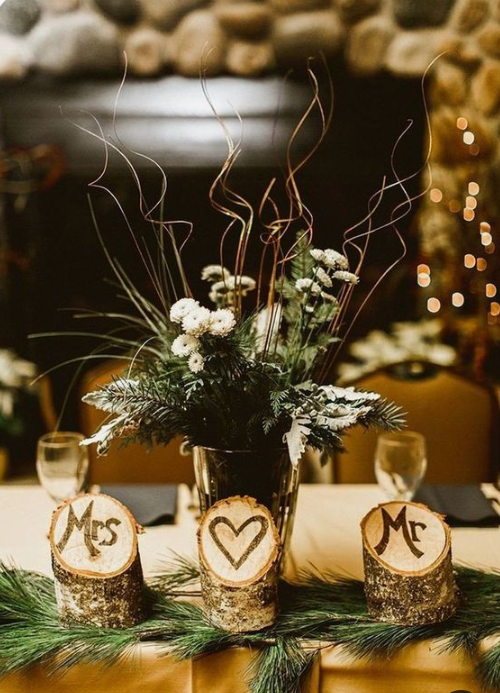 a rustic winter wedding centerpiece of evergreens, tree stumps, a vase with evergreens, blooms and twigs for a rustic winter wedding