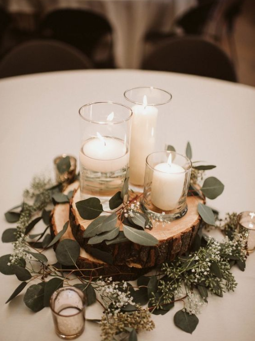 a rustic winter wedding centerpiece of wood slices, greenery and candles in candleholders