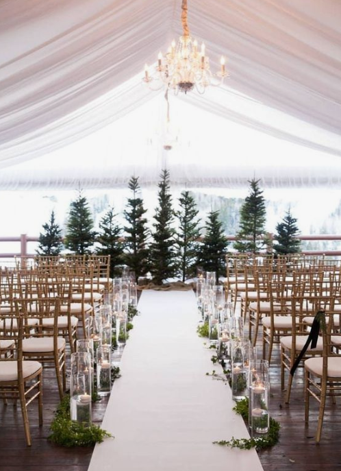 a rustic winter wedding ceremony space with a Christmas tree backdrop, candles in jars and greenery