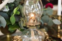 a rustic winter wedding decoration of a wood slice, a lantern and gilded pinecones plus greenery around