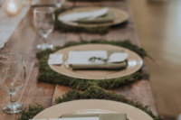 a rustic winter wedding tablescape with moss, gold chargers, evergreens and neutral napkins looks very cozy and very intimate