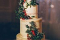 a semi-frosted wedding cake decorated with berries, greenery, pinecones and white blooms for winter