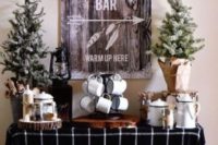 a stylish hot chocolate bar with snowy trees, some metal mugs, lanterns, a snowy sign on the wall and a crate with firewood