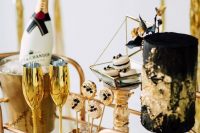 a super cihc and glam bar cart in gold and black with champagne, a fantastic black and gold cake, gold and black lollipops and gold glasses