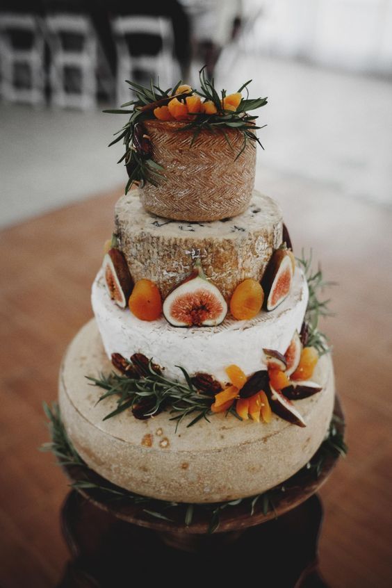 a tall rustic cheese wheel wedding cake topped with fresh fruit and berries plus herbs is a gorgeous idea to rock at the wedding