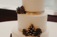 a textural white wedding cake topped with lots of snowy pinecones for a cozy rustic wedding
