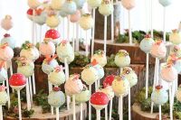 a whimsical stand made of wood slices and moss, with lots of colorful cake popers with sugar blooms and polka dots