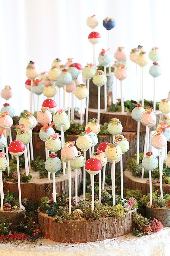 a whimsical stand made of wood slices and moss, with lots of colorful cake popers with sugar blooms and polka dots