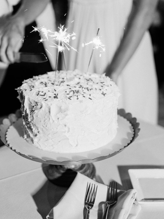 a white buttercream wedding cake topped with confetti and sparklers is a lovely idea for a modern wedding