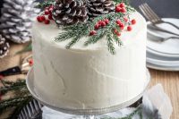 a white buttercream wedding cake topped with snowy pinecones, berries and fir is a stylish rustic idea