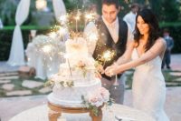 a white textural buttercream wedding cake with blush blooms, greenery and sparklers is a stylish idea for a glam-infused wedding