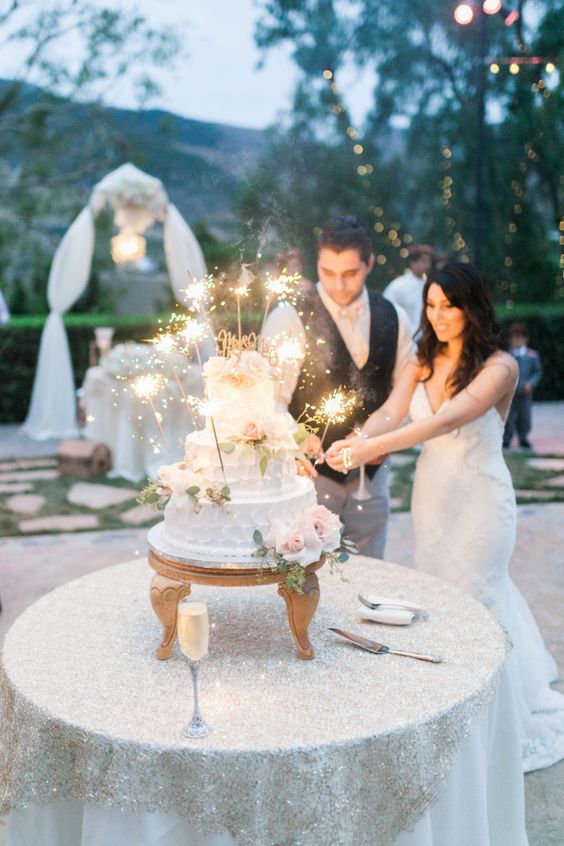 a white textural buttercream wedding cake with blush blooms, greenery and sparklers is a stylish idea for a glam-infused wedding