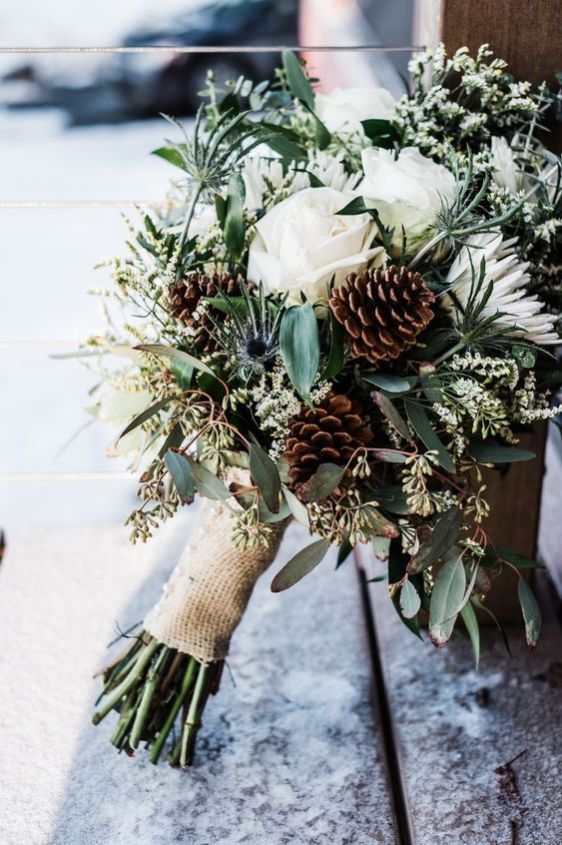 a white wedding bouquet with evergreens, thistles, pinecones and a burlap wrap is very cozy and very cute