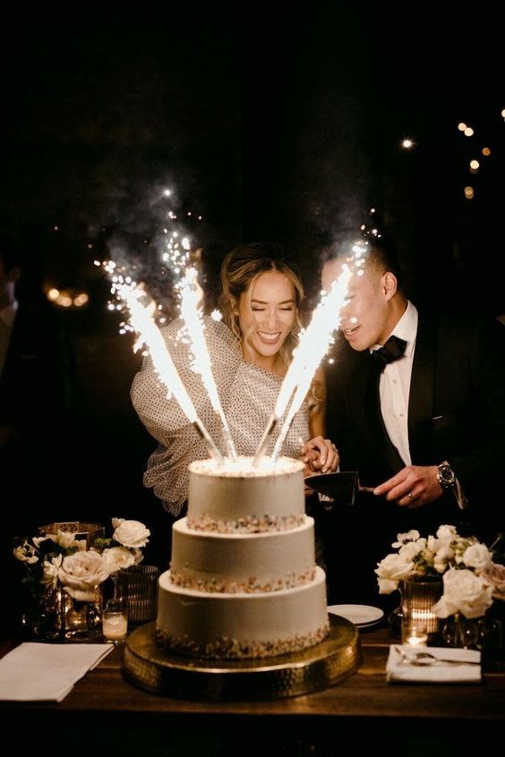 a white wedding cake with confetti and sparklers on top is a gorgeous solution for a party-inspired wedding wiht a touch of fun