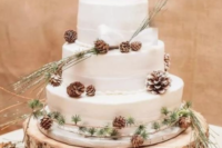 a white wedding cake with white ribbons, pinecones and evergreens looks very cozy and rustic