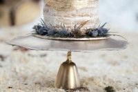 an elegant boho winter wedding cake with gold leaf, thistles and fresh berries on top is a delicious piece